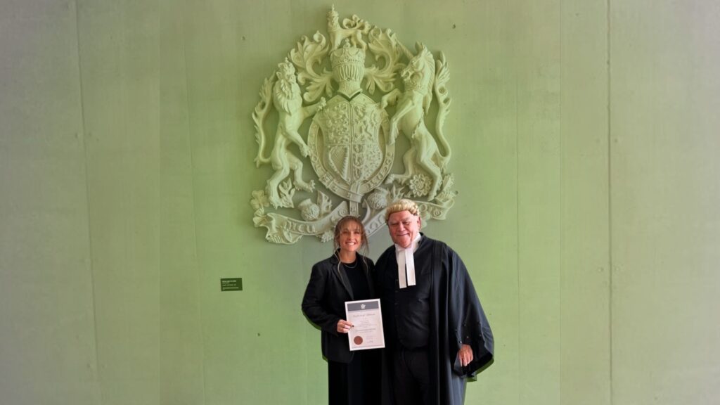 Two people standing in front of a royal coat of arms, celebrating legal achievement with a certificate, representing Green Mortgage Lawyers.